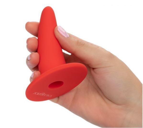 A woman's hand with pale pink nail polish gentle holding what looks like a mini orange road cone made from rubber and with a hole up the middle.