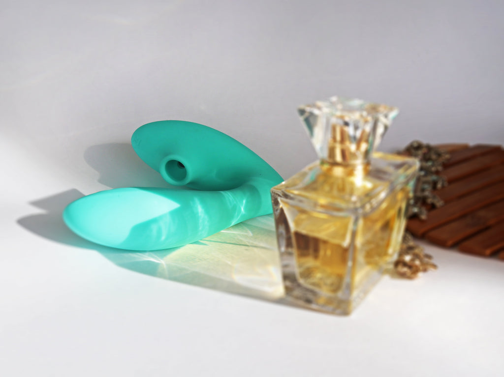A bottle of perfum sitting on a desk in the foreground with a green rubber item laying on it's side behind which is in a U shape with a round suction hole at one end.