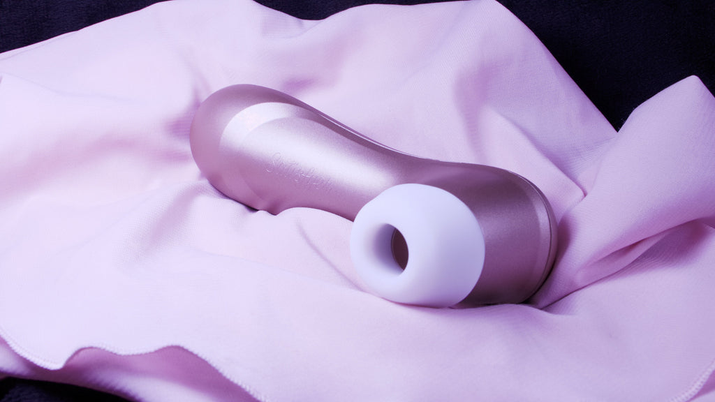 A pale pink sating sheet with a bronze shiny object laying down on it's side on the sheet which has a white rubber nozzle with a hole in the centre.