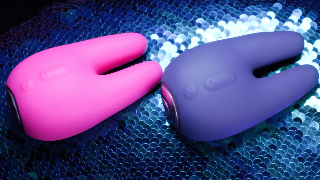 A dark blue shiny sequin background with two identical items which resemble little rabbits laying on top, one above the other, and one in pink and one dark purple.
