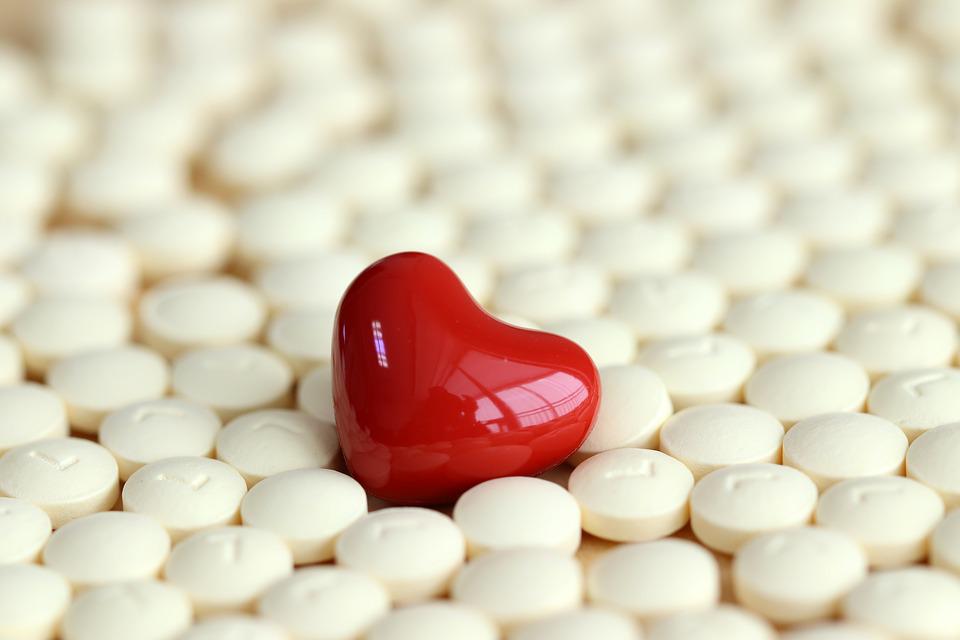 A single bright red heart shaped capsule laying flat on a bed of white tablets covering the ground.