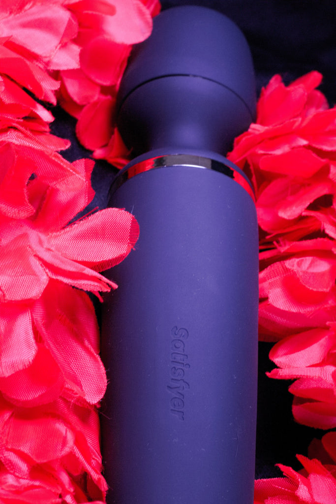A navy blue wand shaped rubber looking object is pictured close up and laying flat on a bed of red flowers. 