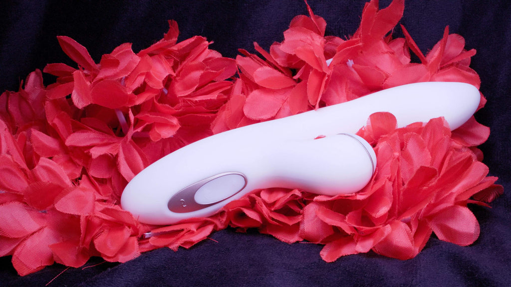 A white and copper coloured product laying down on it's side with the power button visible and on top of bright red flowers.