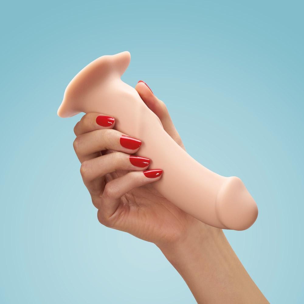 A woman's hand with bright red painted nails holding the skin coloured item with the suction cap facing upwards on a pale blue background.