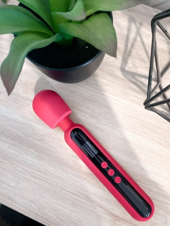 A bright pink wand shaped object is laying flat on a pale wooden bench. The wand is two thirds black and has three pink round buttons about halfway down.