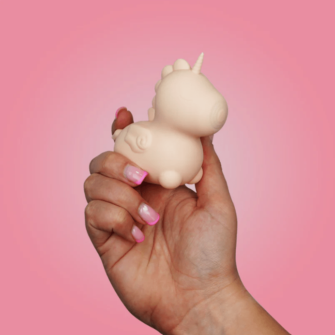 Hand holding a small unicorn figurine against a pink background