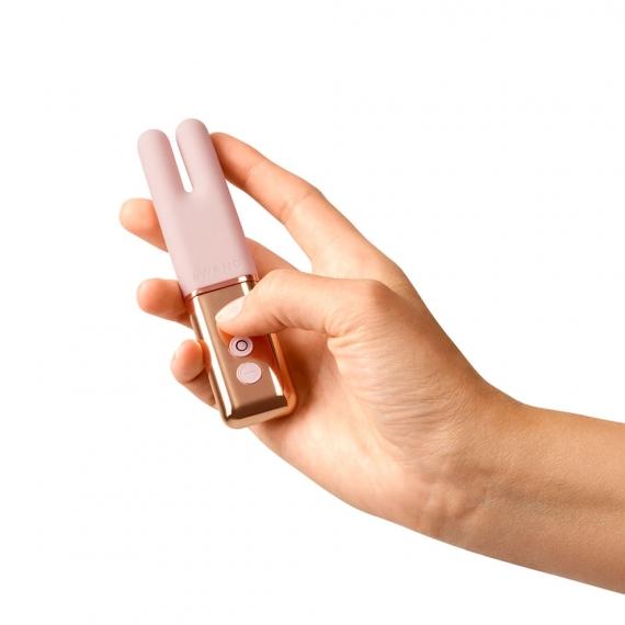 Woman's hand holding a a gold and pink item that is the size of a small remote control but the top has two bunny looking ears and is pink while the bottom half is gold and shiny.